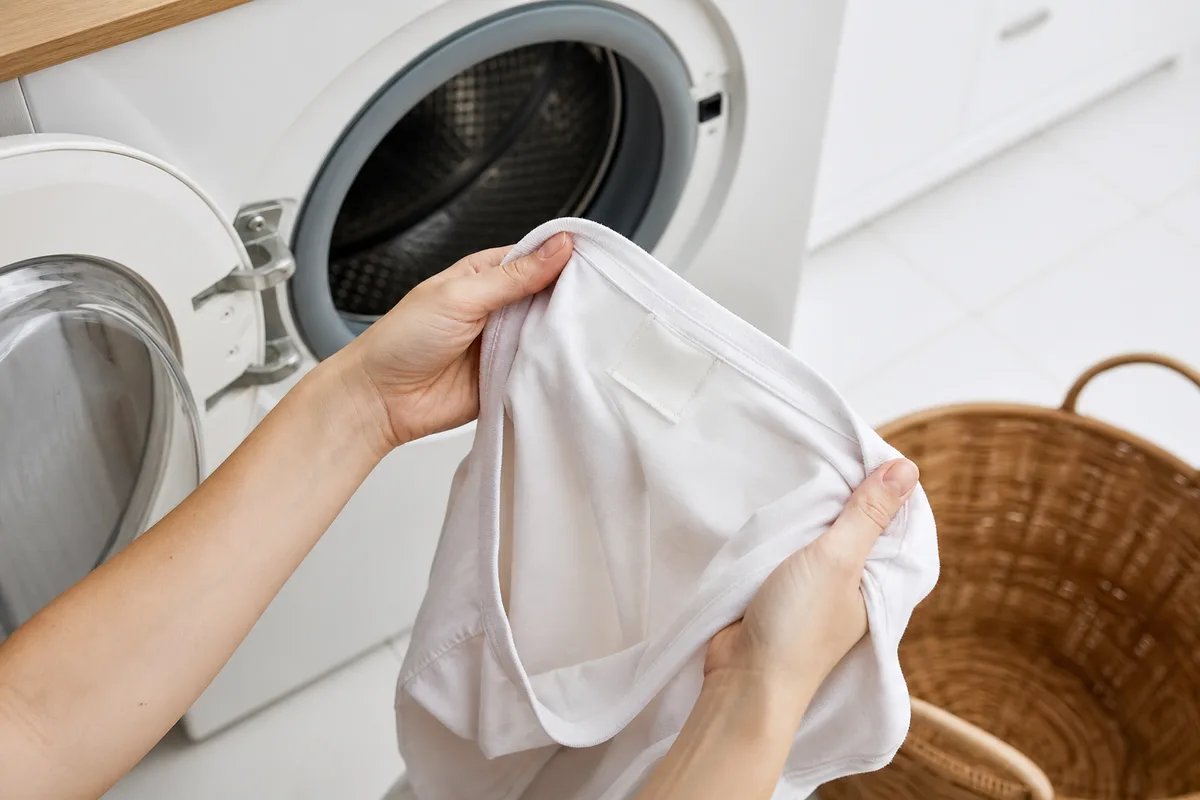 T-shirt retourné sur l&rsquo;envers avant lavage, posé près d&rsquo;un tambour de machine, salle de bain claire